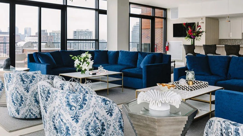 Luxurious lounge area with blue sofas, patterned armchairs, and expansive city views at Astor House Apartments in Chicago
