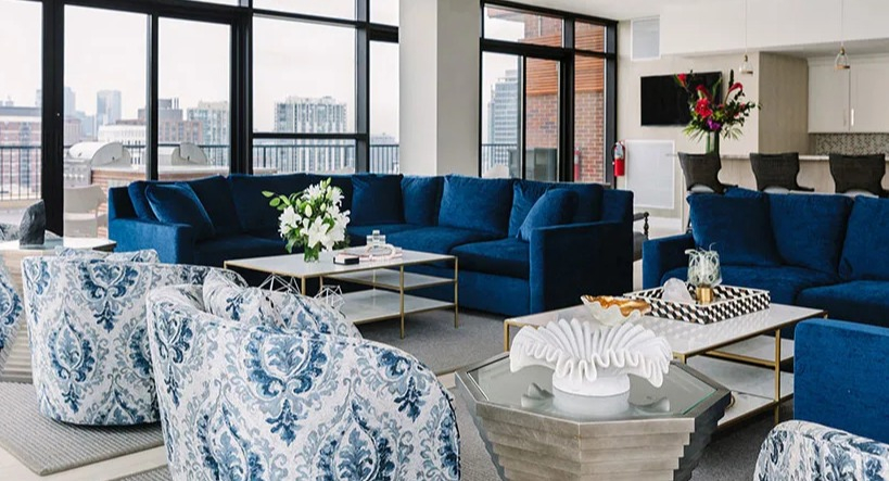 Luxurious lounge area with blue sofas, patterned armchairs, and expansive city views at Astor House Apartments in Chicago