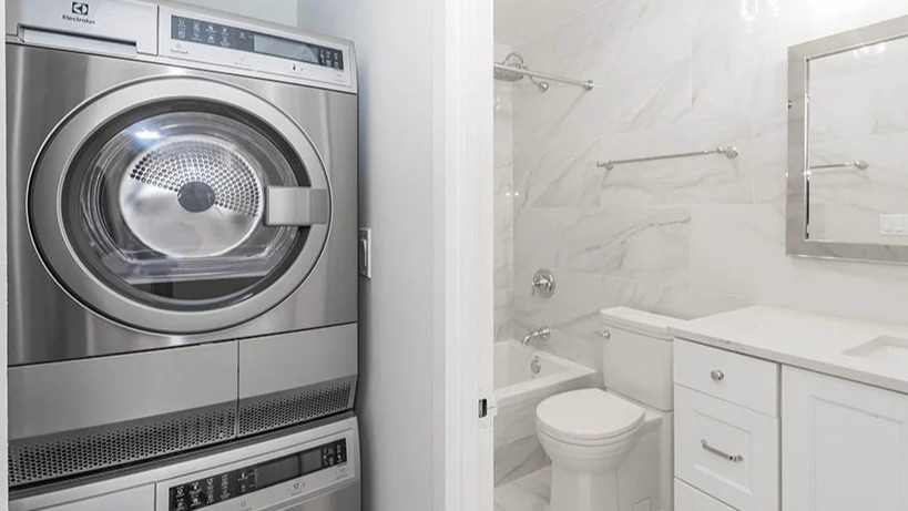 Modern bathroom with white tiling, sleek vanity, and a stacked washer and dryer unit at Astor House Apartments in Chicago