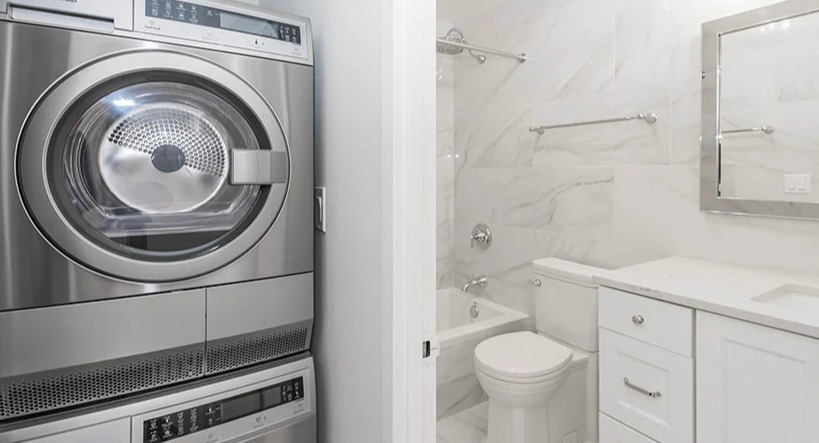 Modern bathroom with white tiling, sleek vanity, and a stacked washer and dryer unit at Astor House Apartments in Chicago