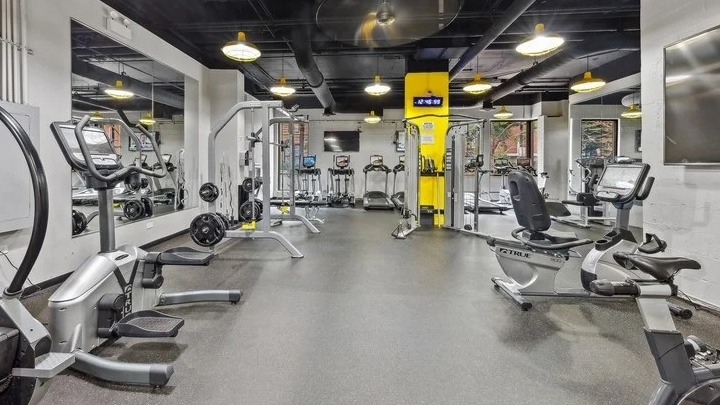 Modern fitness center with various exercise machines, dark flooring, and yellow accents at Astor House Apartments in Chicago