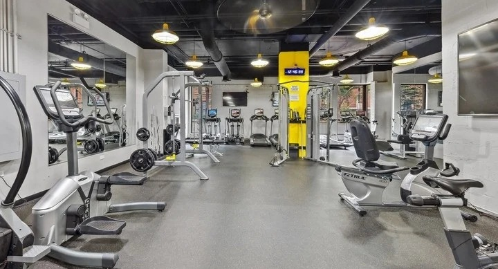 Modern fitness center with various exercise machines, dark flooring, and yellow accents at Astor House Apartments in Chicago