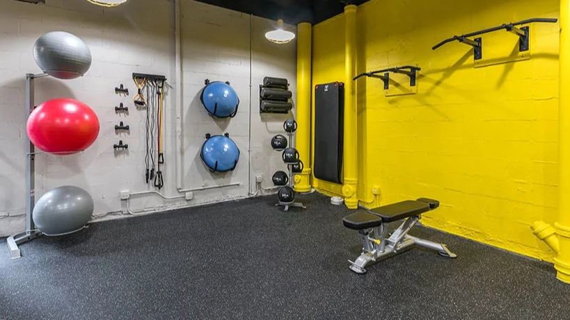 Modern gym and fitness room with bright yellow accents, exercise balls, and weight training equipment at Astor House Apartments in Chicago