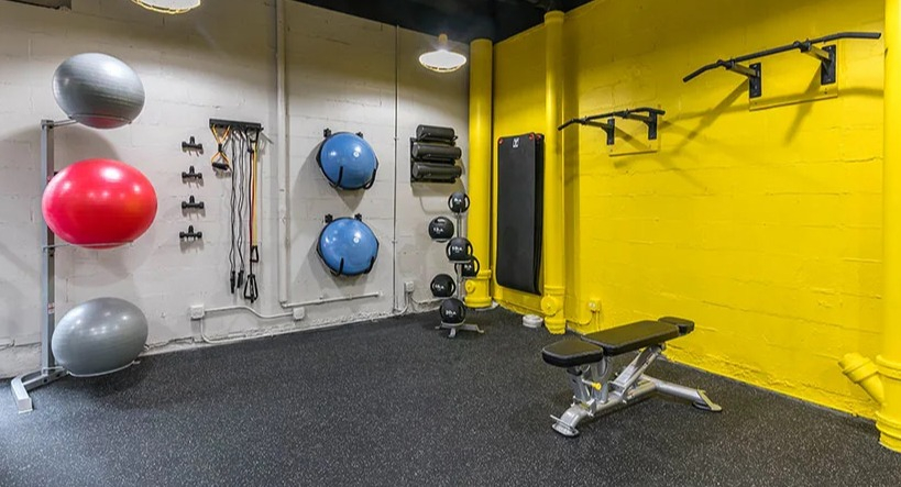 Modern gym and fitness room with bright yellow accents, exercise balls, and weight training equipment at Astor House Apartments in Chicago