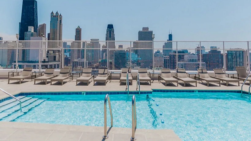 Sparkling rooftop swimming pool with lounge chairs and an impressive view of the Chicago skyline at Astor House Apartments