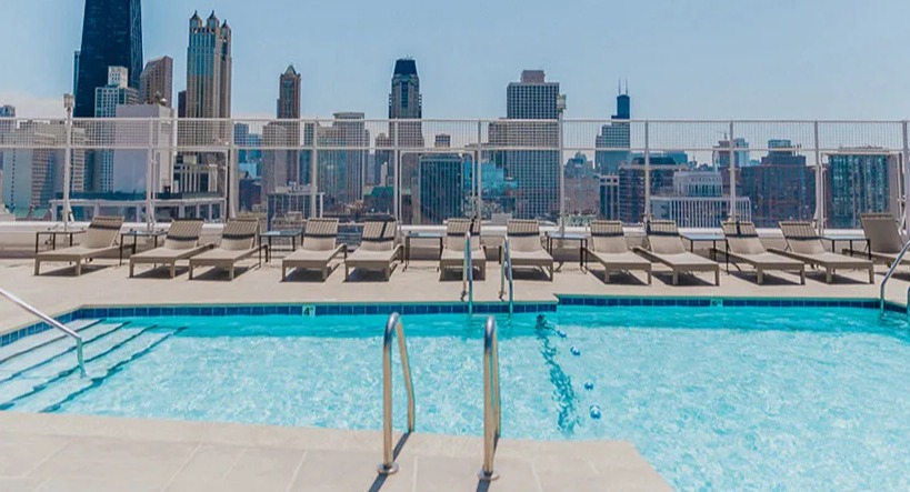 Sparkling rooftop swimming pool with lounge chairs and an impressive view of the Chicago skyline at Astor House Apartments