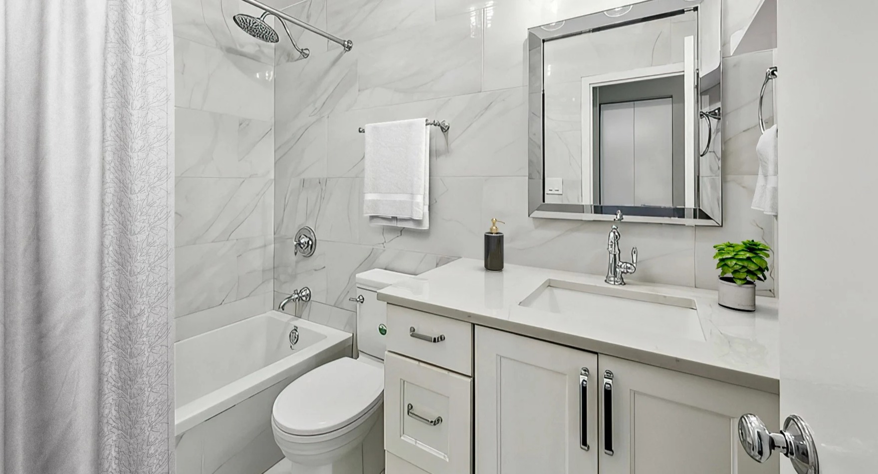 Sleek bathroom with a bathtub, white tiled walls, modern vanity, and reflective mirror at Astor House Apartments in Chicago