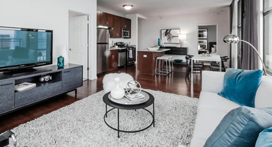 Cozy living room with a white sofa, fluffy rug, entertainment center, and open view to the kitchen at Astoria Tower Chicago
