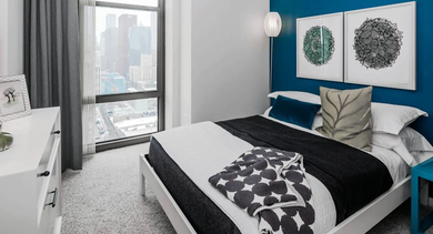 Vibrant bedroom with a blue accent wall, modern bed, and large window offering a city view at Astoria Tower Chicago apartments
