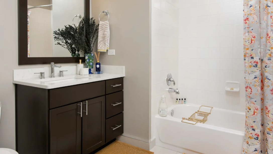 Modern bathroom at Atwater Apartments in Chicago, featuring a dark wood vanity, white tiles, and a vibrant, colorful shower curtain
