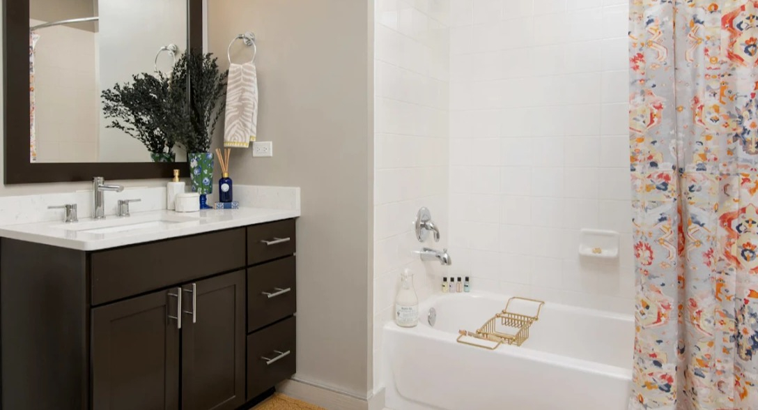 Modern bathroom at Atwater Apartments in Chicago, featuring a dark wood vanity, white tiles, and a vibrant, colorful shower curtain