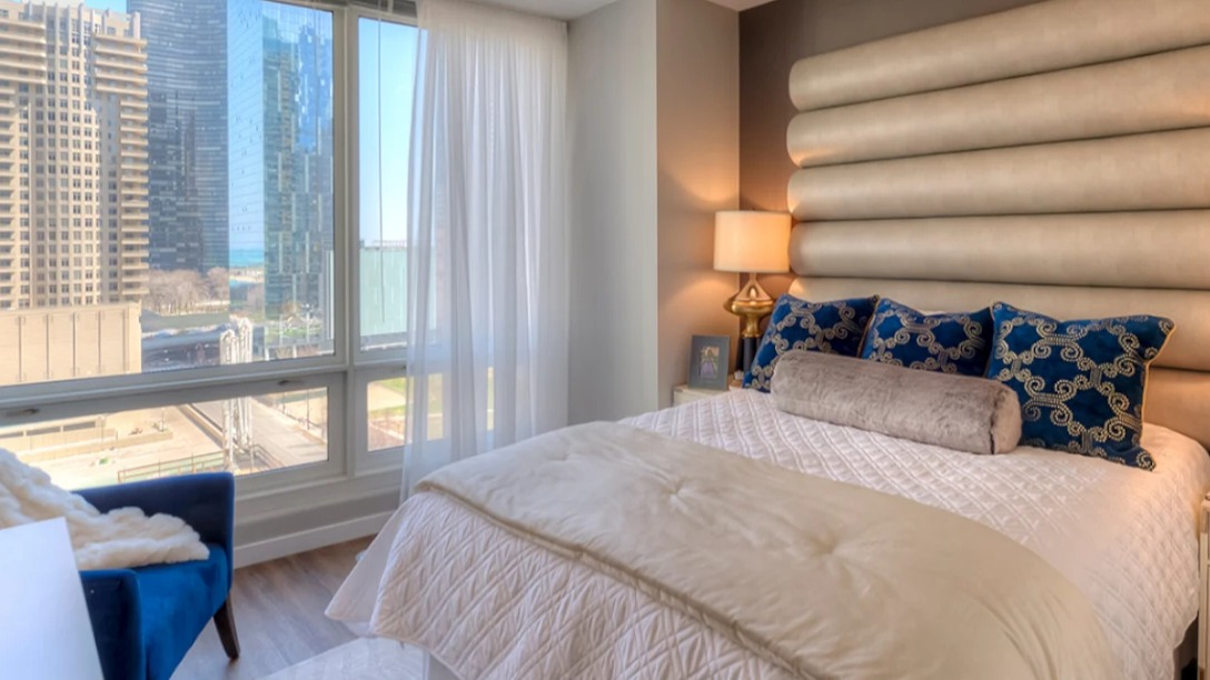 Luxurious bedroom at Atwater Apartments in Chicago, featuring a plush bed, elegant headboard, and expansive city views