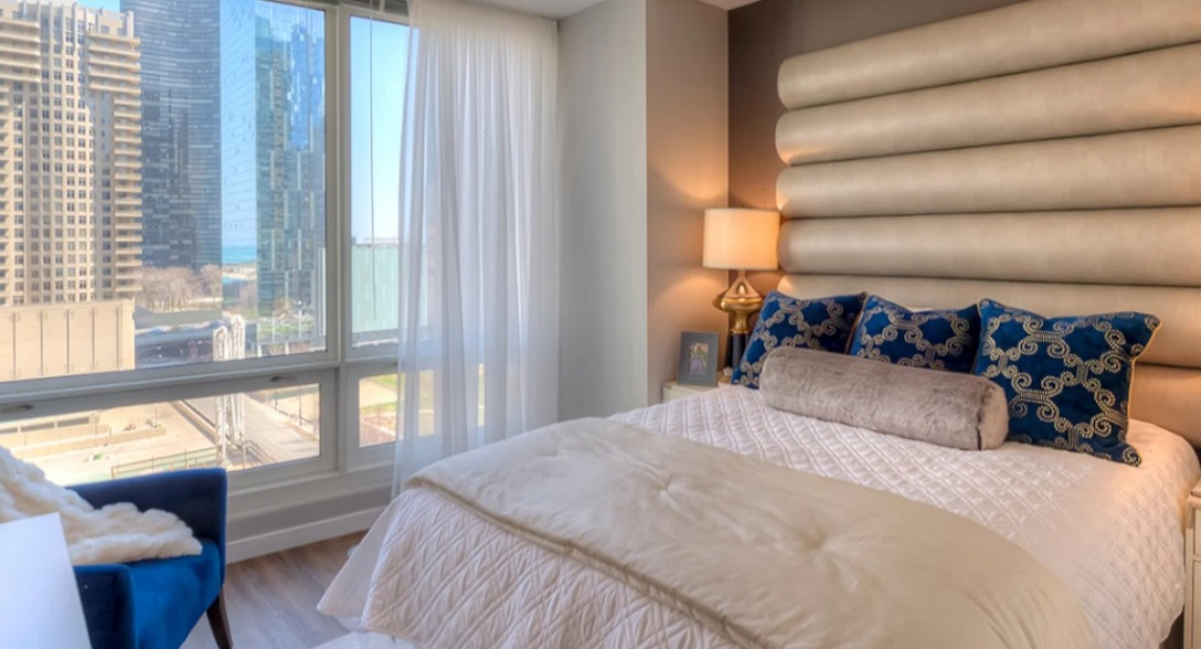 Luxurious bedroom at Atwater Apartments in Chicago, featuring a plush bed, elegant headboard, and expansive city views