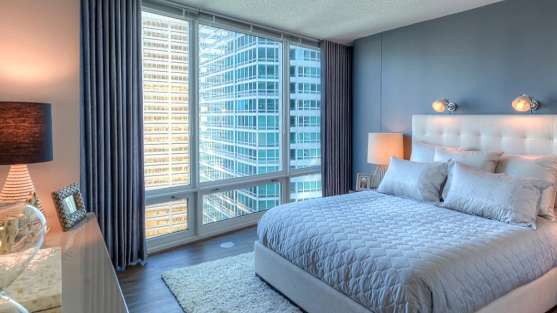 Luxurious bedroom at Atwater Apartments in Chicago, featuring a comfortable bed, elegant decor, and expansive city views from floor-to-ceiling windows