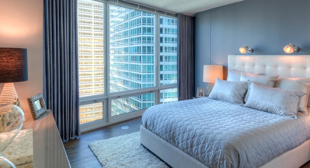 Luxurious bedroom at Atwater Apartments in Chicago, featuring a comfortable bed, elegant decor, and expansive city views from floor-to-ceiling windows