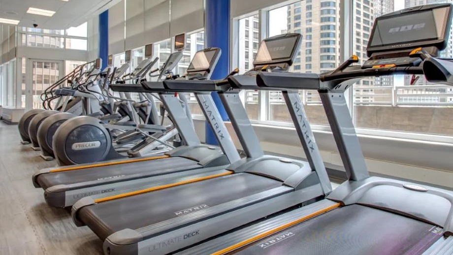 State-of-the-art fitness center with a row of modern treadmills and ellipticals, offering city views through large windows at Atwater Apartments in Chicago