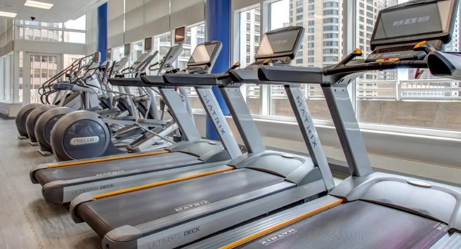 State-of-the-art fitness center with a row of modern treadmills and ellipticals, offering city views through large windows at Atwater Apartments in Chicago