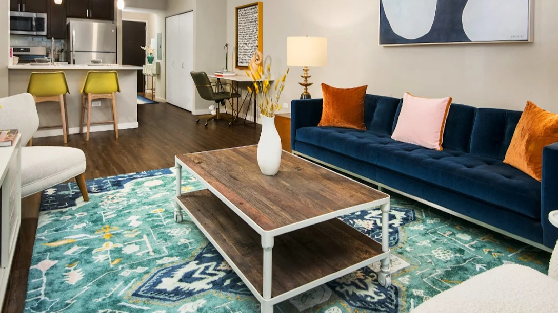 Vibrant living room at Atwater Apartments in Chicago, featuring a colorful rug, comfortable seating, and an adjacent kitchen