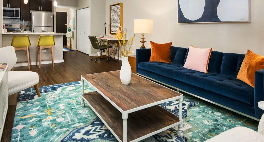 Vibrant living room at Atwater Apartments in Chicago, featuring a colorful rug, comfortable seating, and an adjacent kitchen