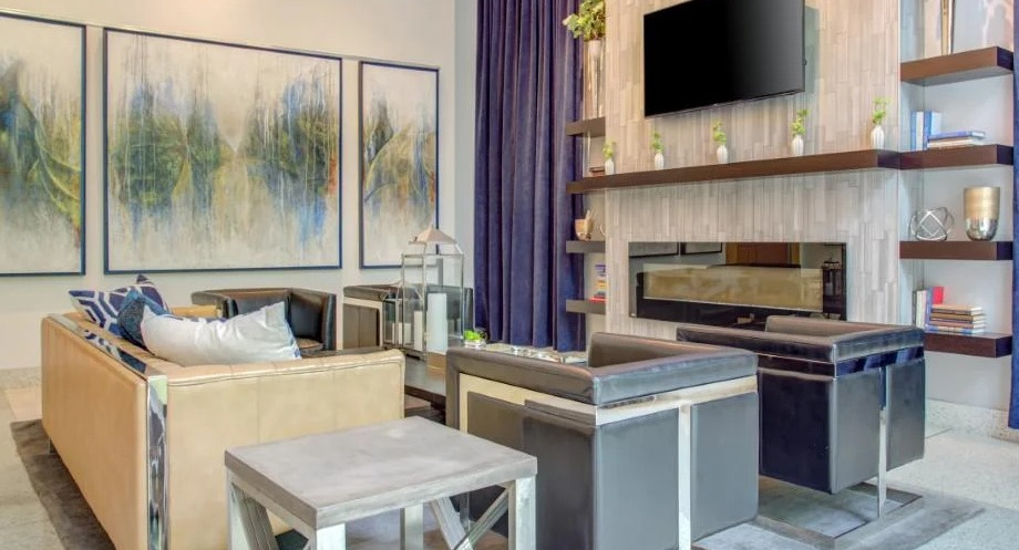 Luxurious resident lounge with comfortable seating, a modern fireplace, wall-mounted TV, and elegant blue drapes at Atwater Apartments in Chicago