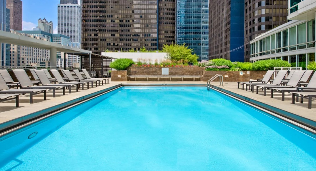 Outdoor swimming pool at Atwater Apartments in Chicago, featuring lounge chairs and a stunning city skyline backdrop