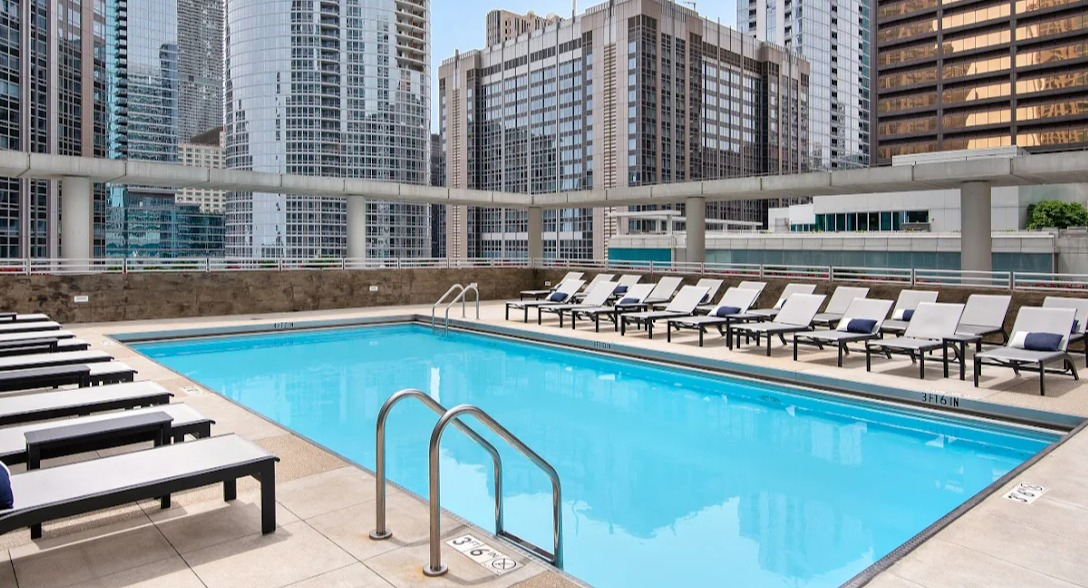Sparkling outdoor swimming pool at Atwater Apartments in Chicago, surrounded by lounge chairs and a dramatic city skyline backdrop