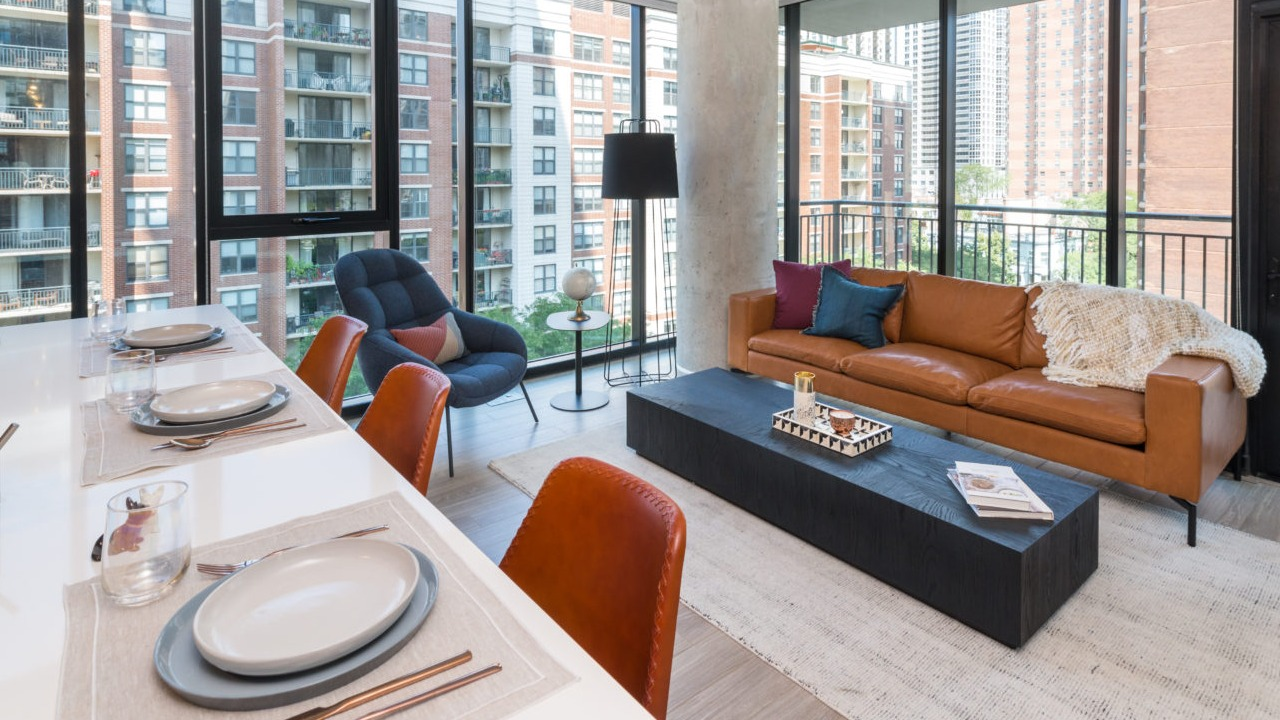 A stylish apartment living room with a brown leather sofa, large windows, and an outdoor balcony view in Chicago