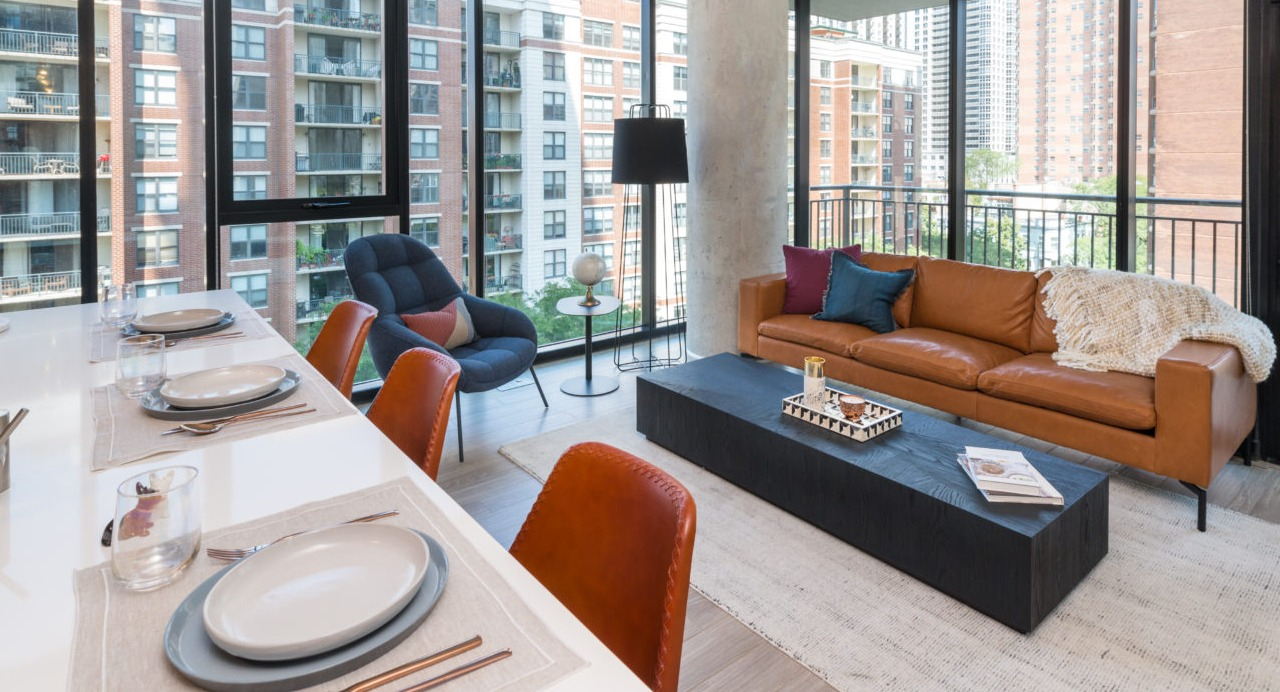 A stylish apartment living room with a brown leather sofa, large windows, and an outdoor balcony view in Chicago