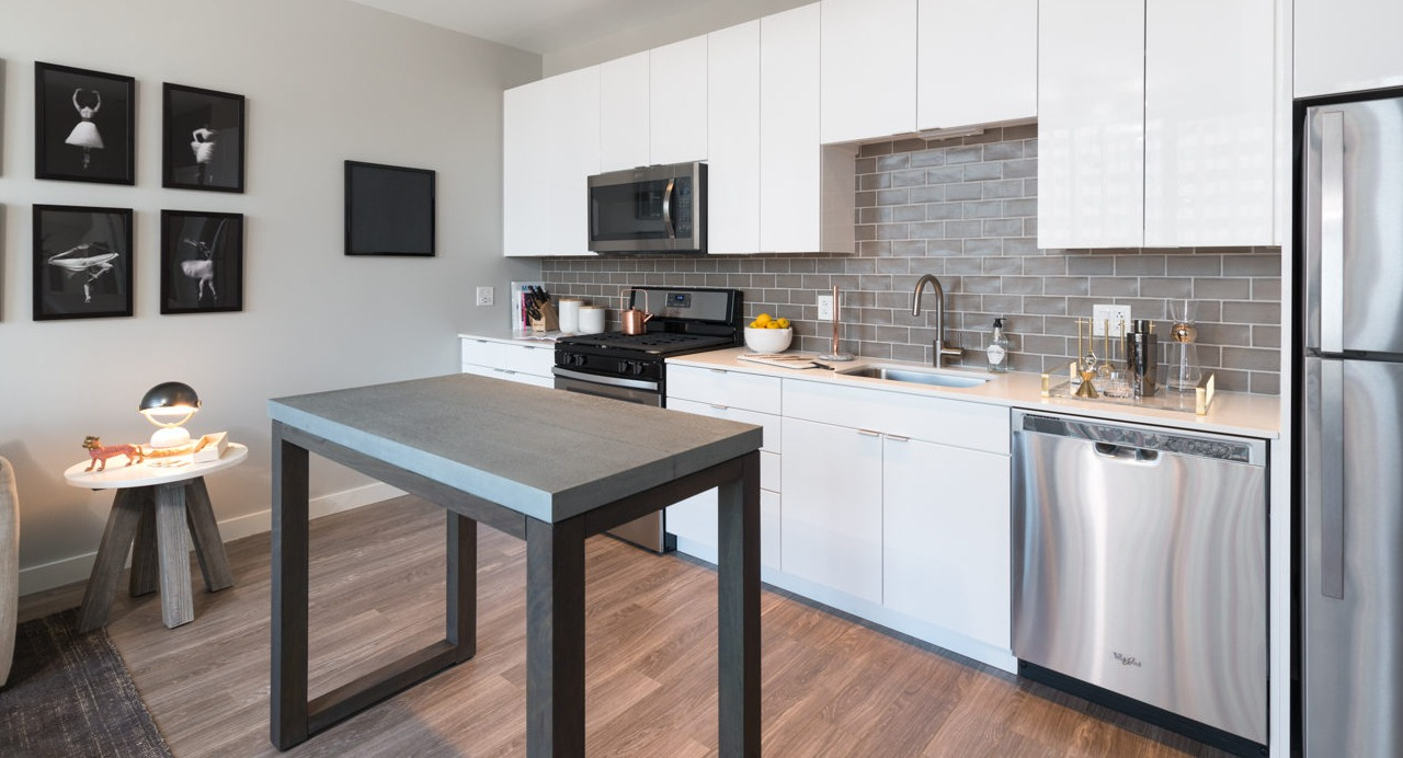 A sleek and modern kitchen with white cabinets, stainless steel appliances, and a compact dining area