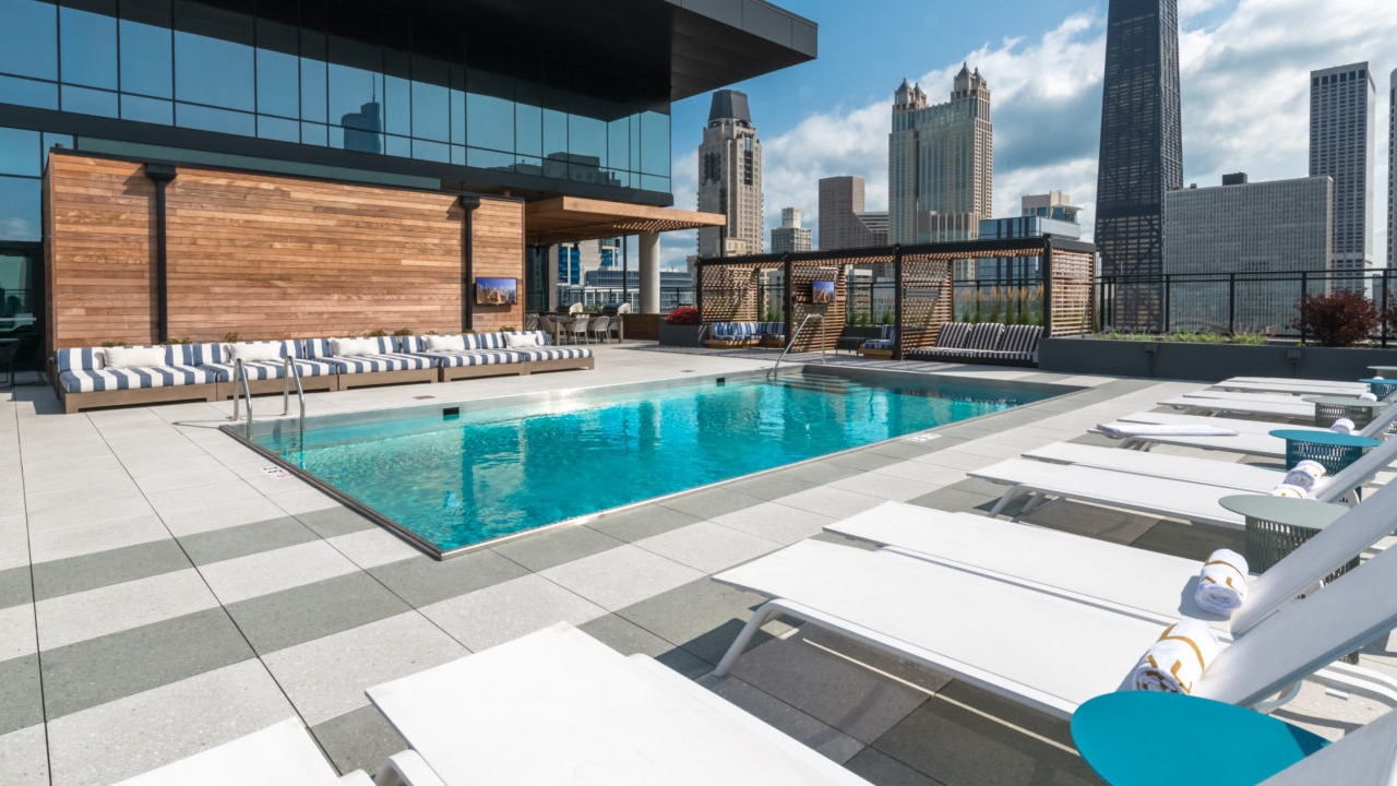 A luxurious rooftop pool area with lounge chairs and the Chicago skyline visible in the background on a sunny day