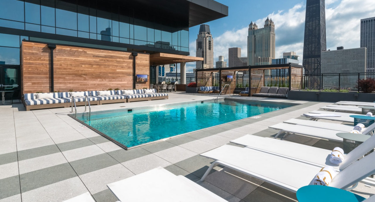 A luxurious rooftop pool area with lounge chairs and the Chicago skyline visible in the background on a sunny day