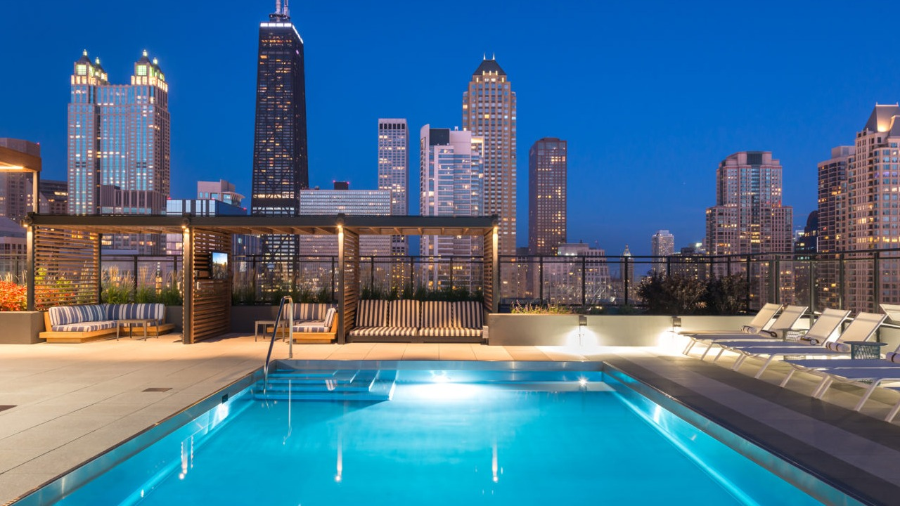 A serene rooftop pool area illuminated at night, with the sparkling Chicago city lights in the background