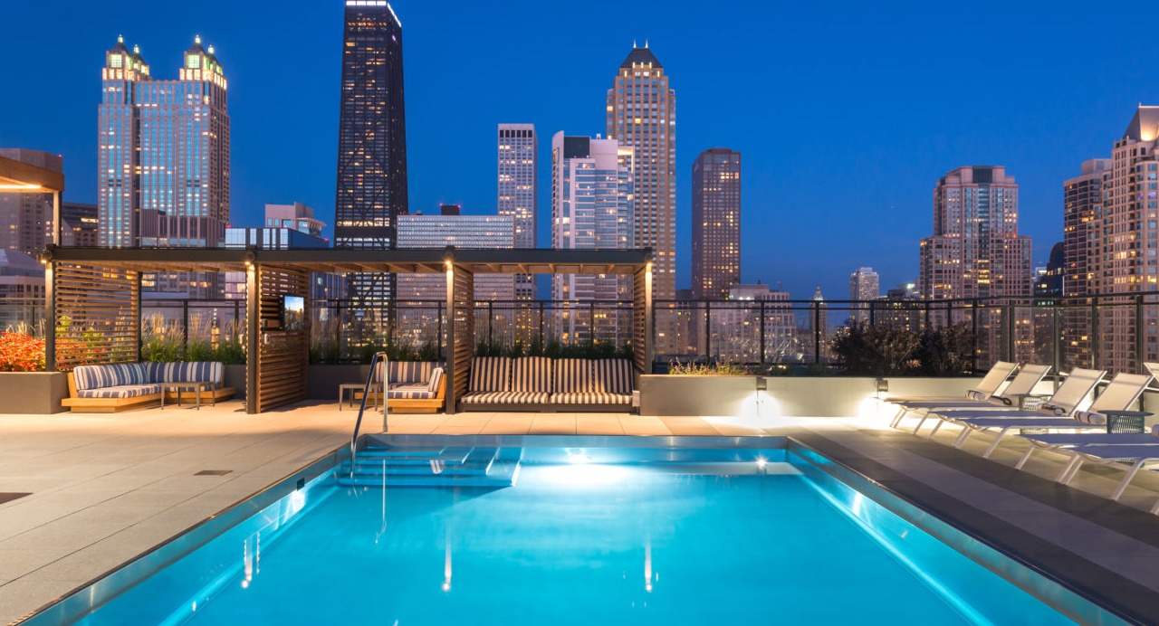 A serene rooftop pool area illuminated at night, with the sparkling Chicago city lights in the background