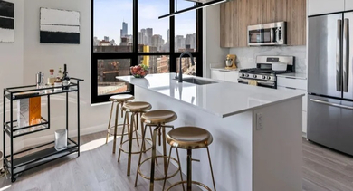 Modern apartment kitchen with a large island, bar stools, stainless steel appliances, and a stylish bar cart at Avenir apartments in Chicago