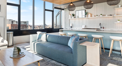 Bright resident lounge with a contemporary kitchen, bar seating, a cozy blue sofa, and large windows at Avenir apartments in Chicago