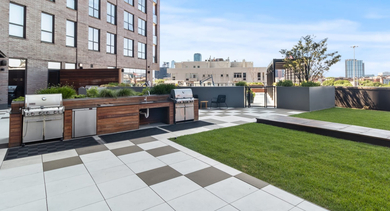 A modern rooftop grilling station with built-in BBQs and a green lawn, offering city views at Avenir apartments in Chicago