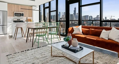 A spacious living room with an orange sofa, dining area, modern kitchen, and expansive city views at Avenir apartments in Chicago