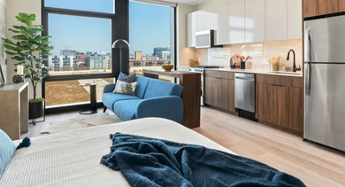 A stylish studio apartment with a blue sofa, kitchen, and city views at Avra West Loop in Chicago