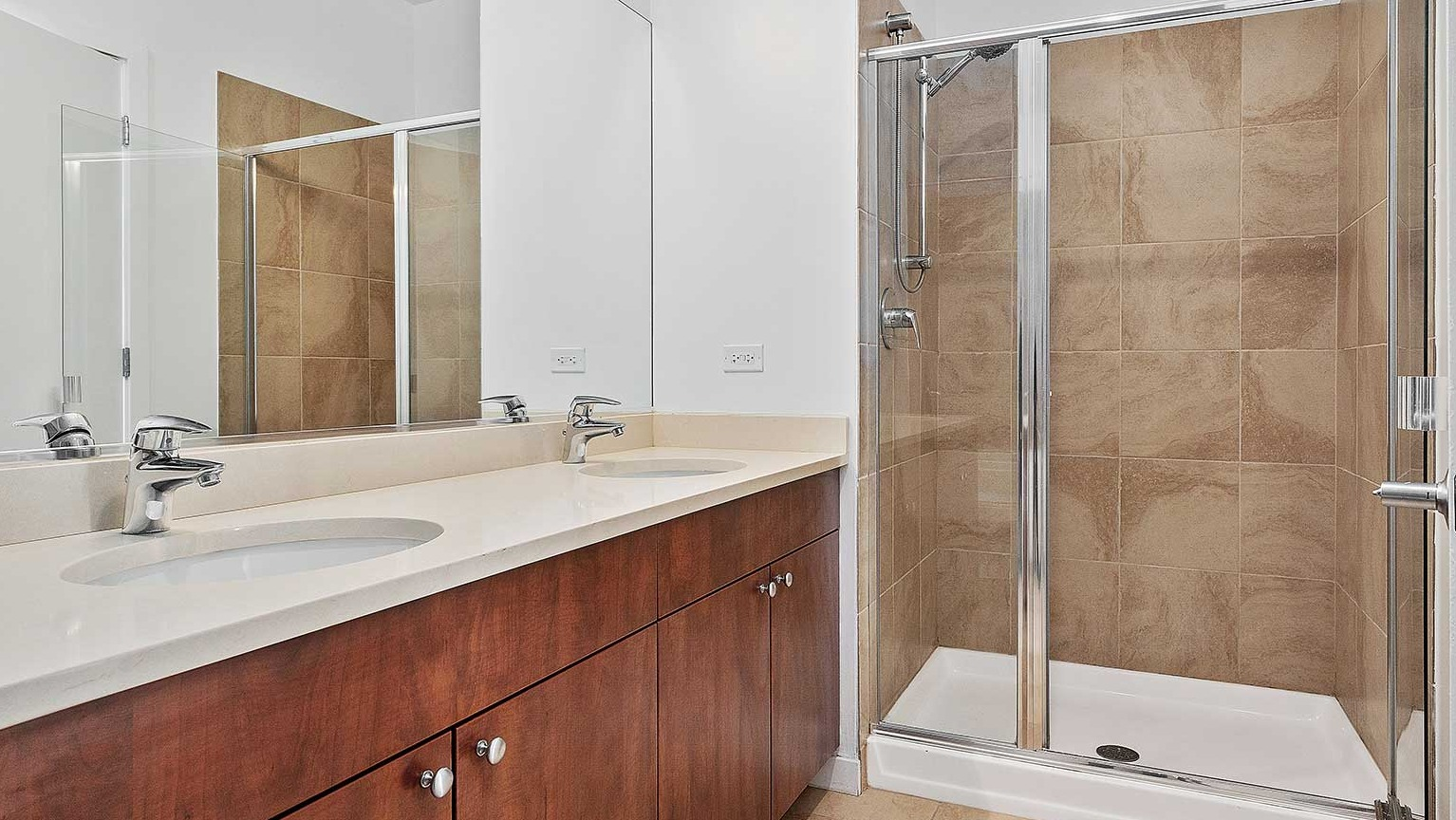 Modern bathroom featuring a double vanity, a spacious walk-in shower with glass doors, and light-colored tiles at Burnham Pointe in Chicago