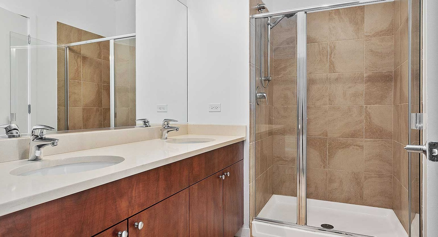 Modern bathroom featuring a double vanity, a spacious walk-in shower with glass doors, and light-colored tiles at Burnham Pointe in Chicago