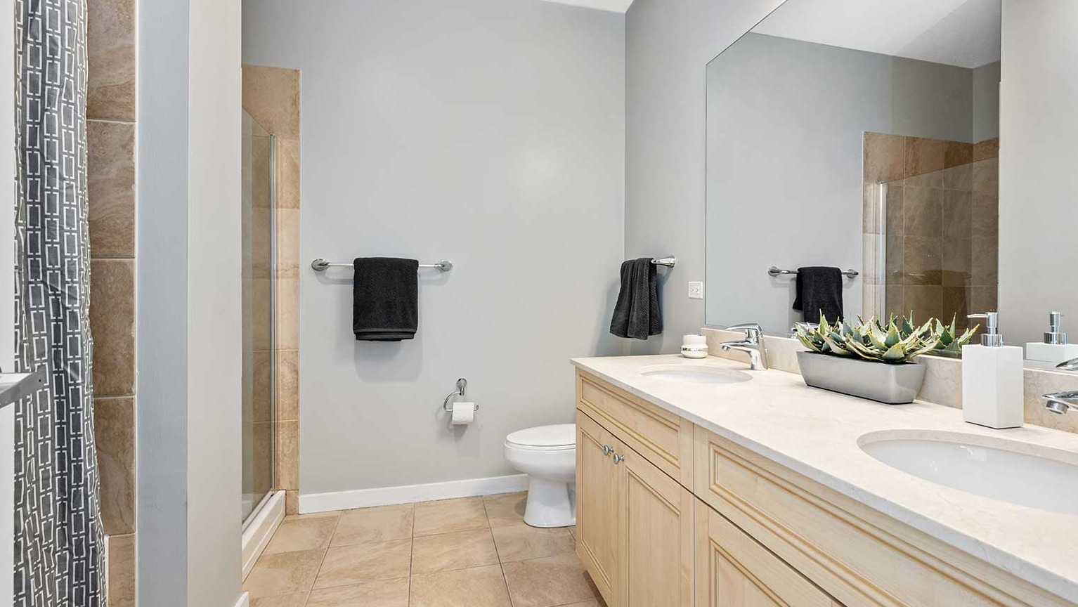 Elegant bathroom with dual sinks, a large mirror, and a walk-in shower with a modern curtain at Burnham Pointe apartments in Chicago