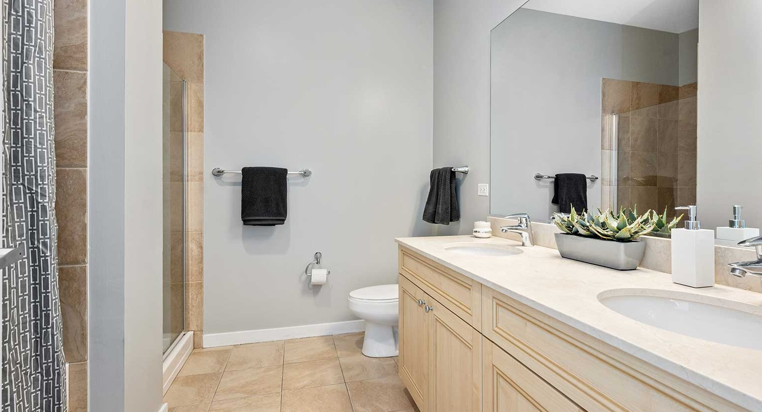 Elegant bathroom with dual sinks, a large mirror, and a walk-in shower with a modern curtain at Burnham Pointe apartments in Chicago