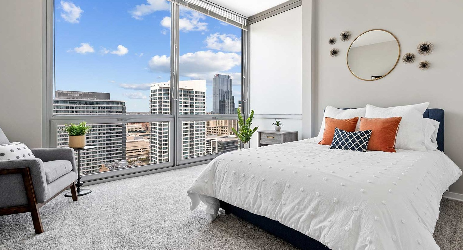Inviting bedroom with plush carpeting, a comfortable bed, stylish decor, and large windows offering city views at Burnham Pointe in Chicago