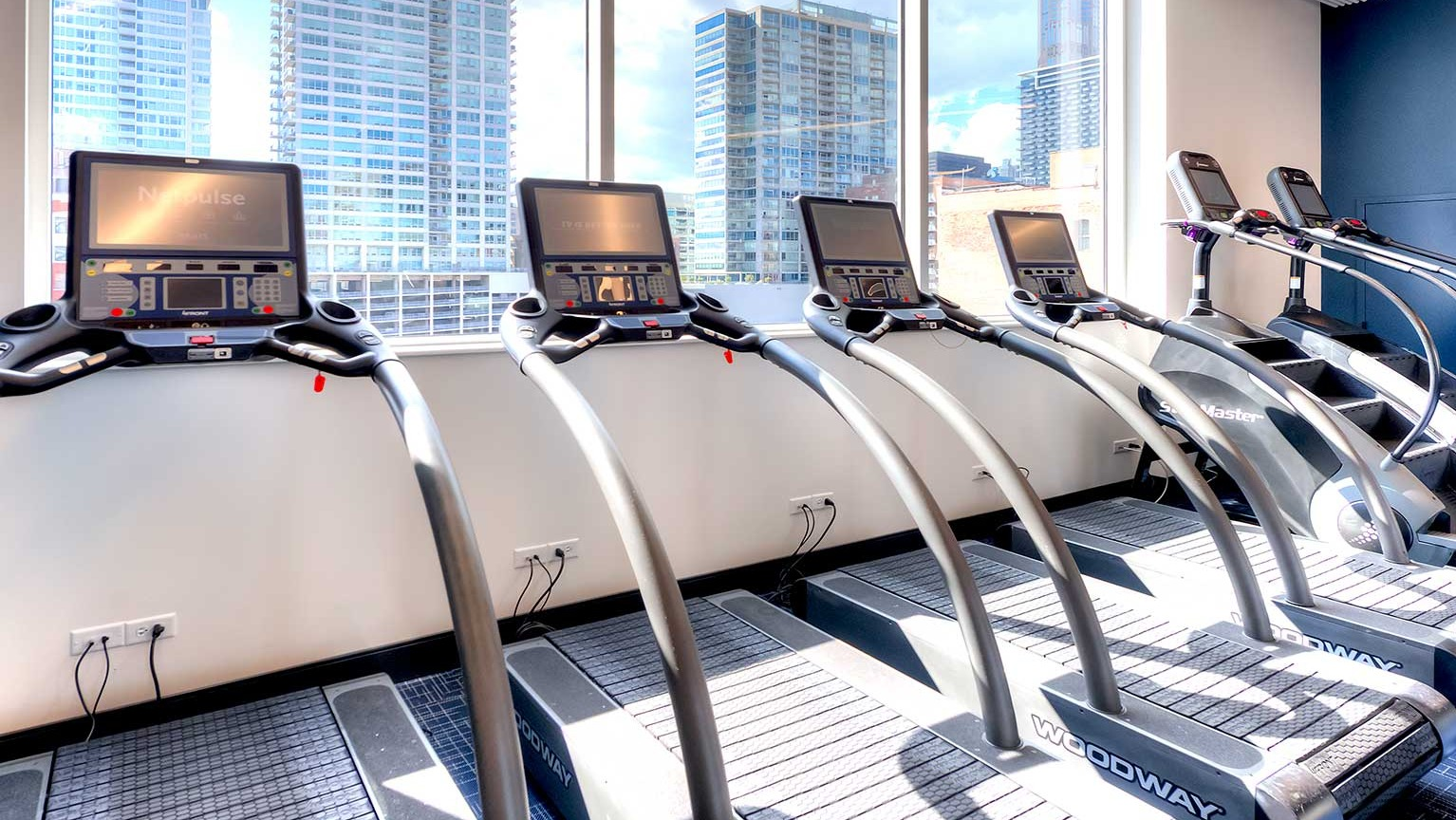 Row of modern treadmills with individual screens, offering city views through large windows in the gym at Burnham Pointe in Chicago