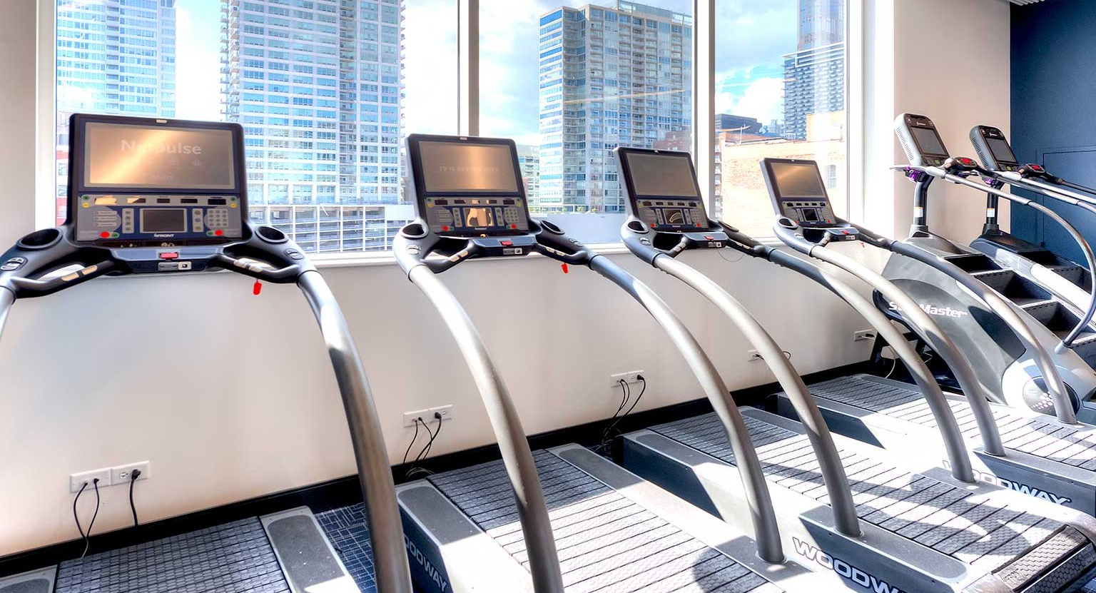 Row of modern treadmills with individual screens, offering city views through large windows in the gym at Burnham Pointe in Chicago
