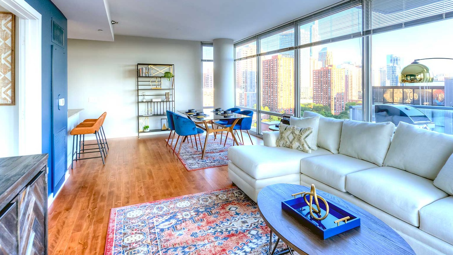 Bright living and dining area with a white sectional, colorful rug, and floor-to-ceiling windows offering city views at Burnham Pointe in Chicago