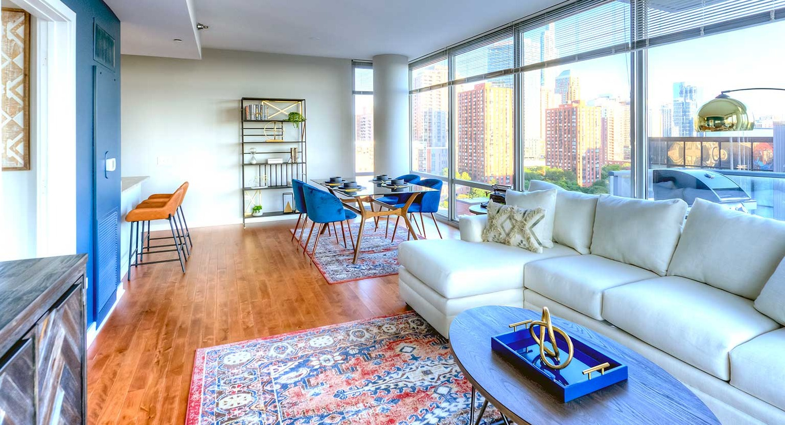 Bright living and dining area with a white sectional, colorful rug, and floor-to-ceiling windows offering city views at Burnham Pointe in Chicago
