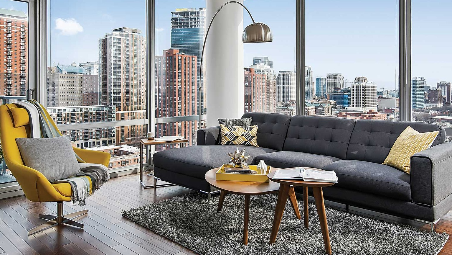 Elegant living room with a large sectional sofa, a cozy yellow chair, and expansive city views from large windows at Burnham Pointe in Chicago