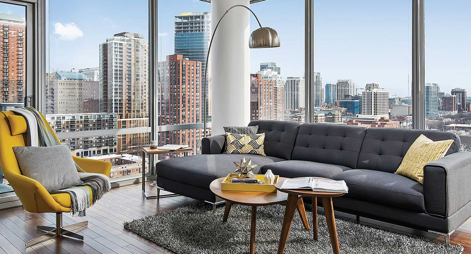 Elegant living room with a large sectional sofa, a cozy yellow chair, and expansive city views from large windows at Burnham Pointe in Chicago