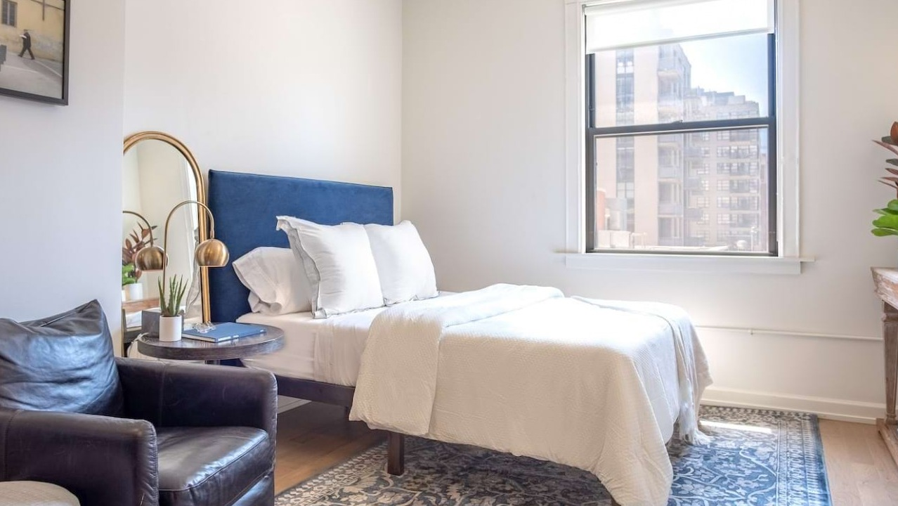 Bright bedroom at The Bush Temple in Chicago, featuring a comfortable bed, stylish decor, and a large window overlooking the city